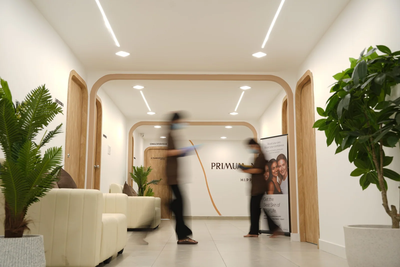 The clinic corridor: white walls, arched timber doors, soft seating and plants leading to the consultation room
