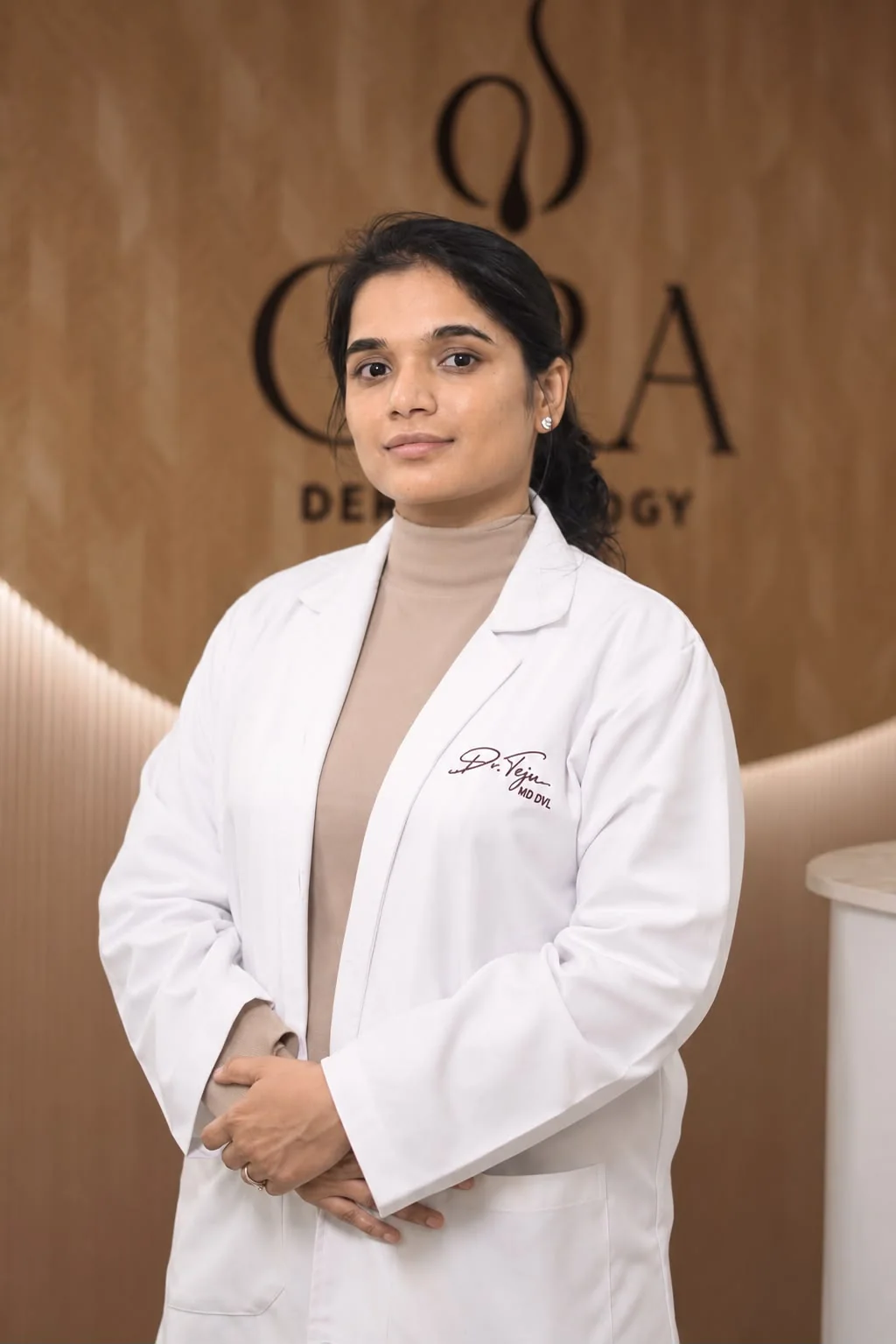 Dr. Tejaswi Kothapally in a white coat in front of the Cyra Dermatology wall